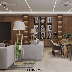 Living room featuring a ceiling fan with woven blades hanging from the ceiling. A brown leather couch sits on a woven jute rug. Two brown accent chairs flank a round wooden coffee table with a black metal base. Text overlay: Houme India - Interior Design Ideas. B